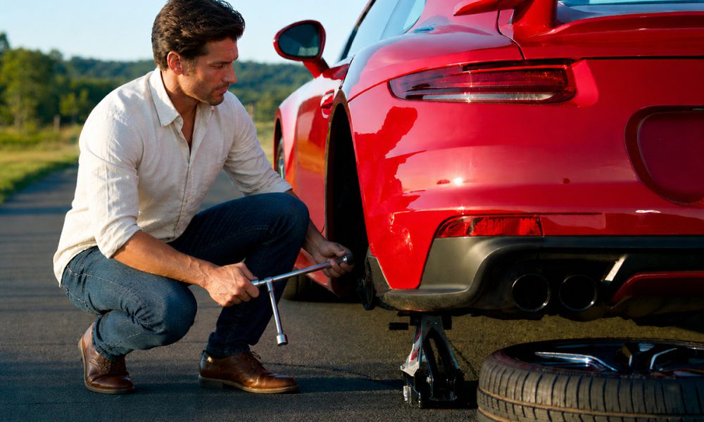 Man Changing A Flat Tire On The Side Of The Road
